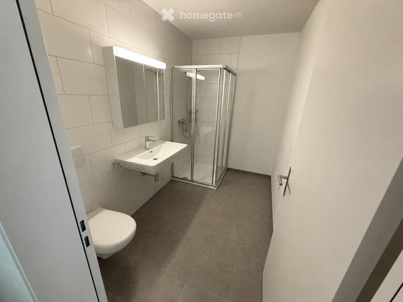Modern bathroom with white tiles, a toilet, a sink with a mirror, and a glass-enclosed shower stall.