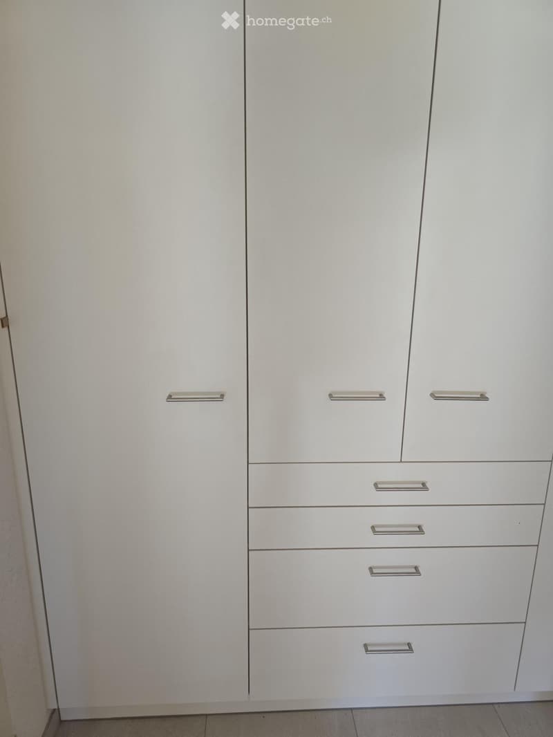 Empty room with white built-in wardrobes and drawers, featuring sleek silver handles.