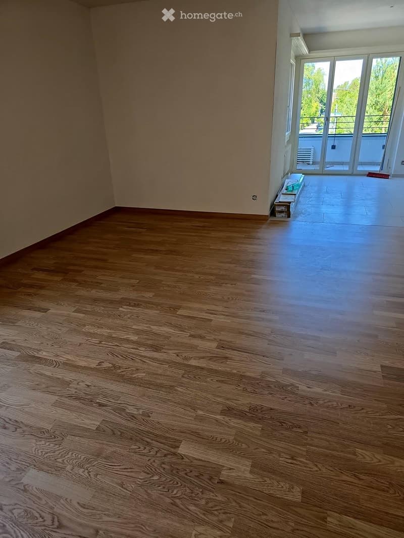 Empty room with wooden flooring and large windows leading to a balcony. No furniture or equipment visible.