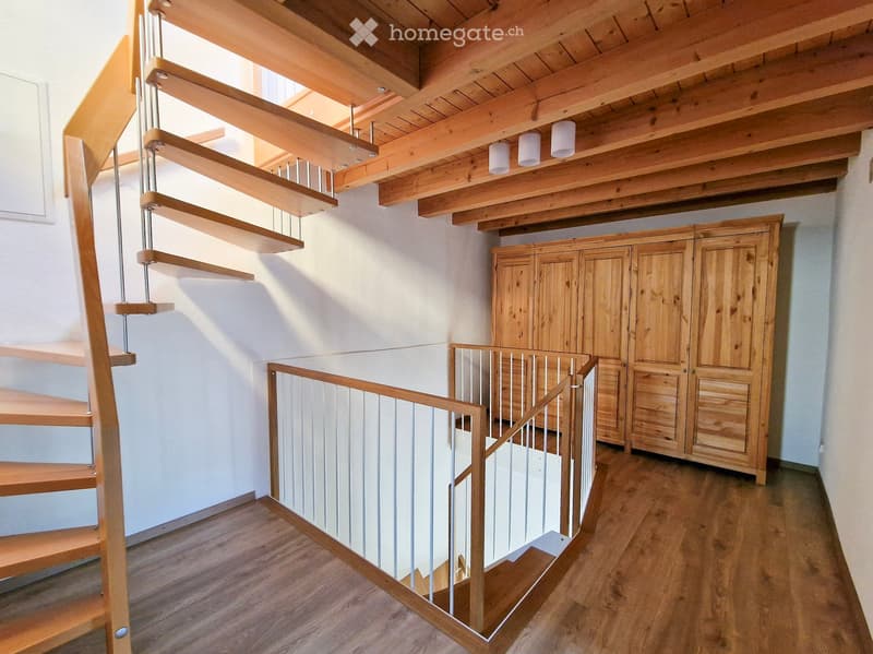 Spiral staircase with wooden steps and metal railing, wooden cabinets, exposed wooden ceiling beams, and recessed lighting.