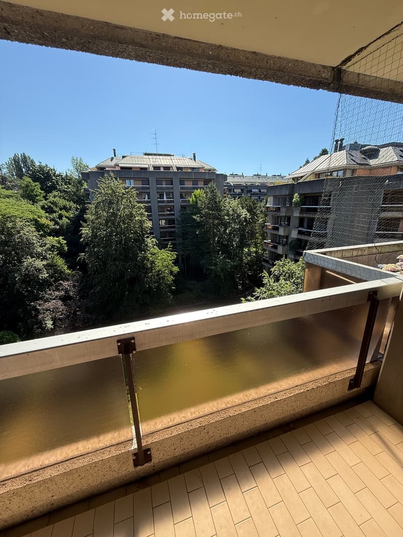 Balcony with tiled floor, metal railing, and a view of surrounding buildings and greenery.