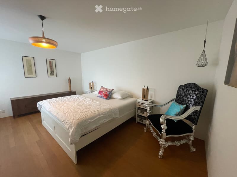 A well-lit bedroom with a white bed, a decorative chair, nightstands, and artwork on the walls.