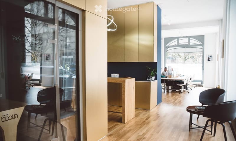 Modern office space with light wood flooring, glass walls, and contemporary furniture including chairs, tables, and a cabinet.