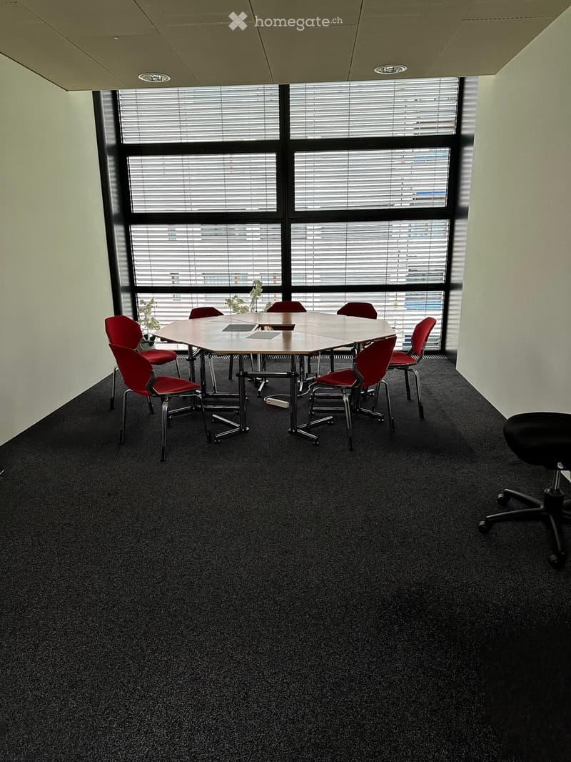 round table, red chairs, carpeted floor, large windows with blinds