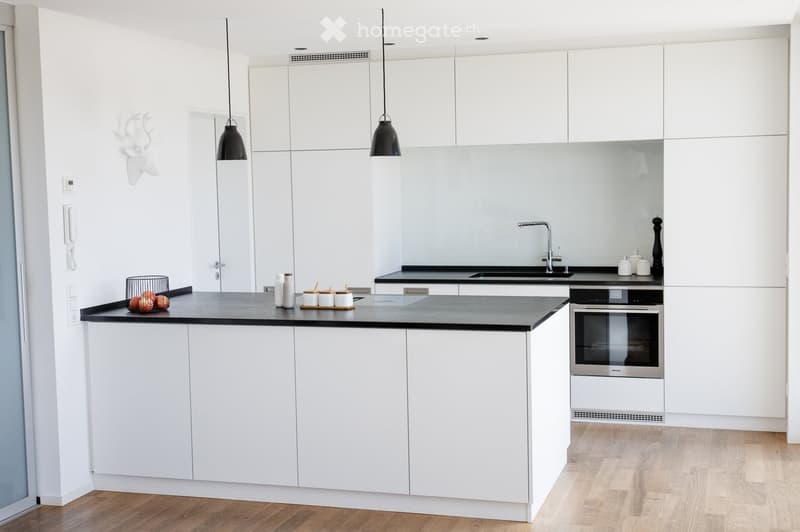 Modern kitchen with white cabinets, black countertops, and a central island. Features include a sink with a modern faucet, an oven, pendant lights, and decorative items on the counter.