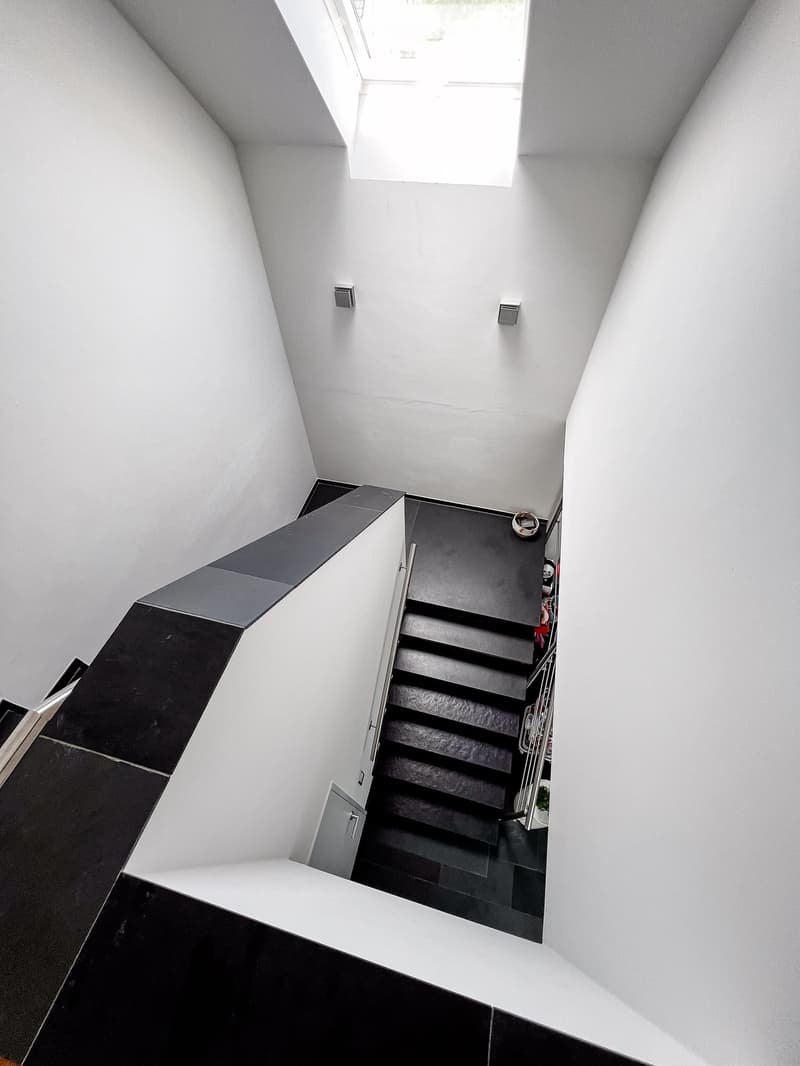 Modern, minimalist staircase with black steps and white walls, featuring a skylight at the top and built-in storage on one side.