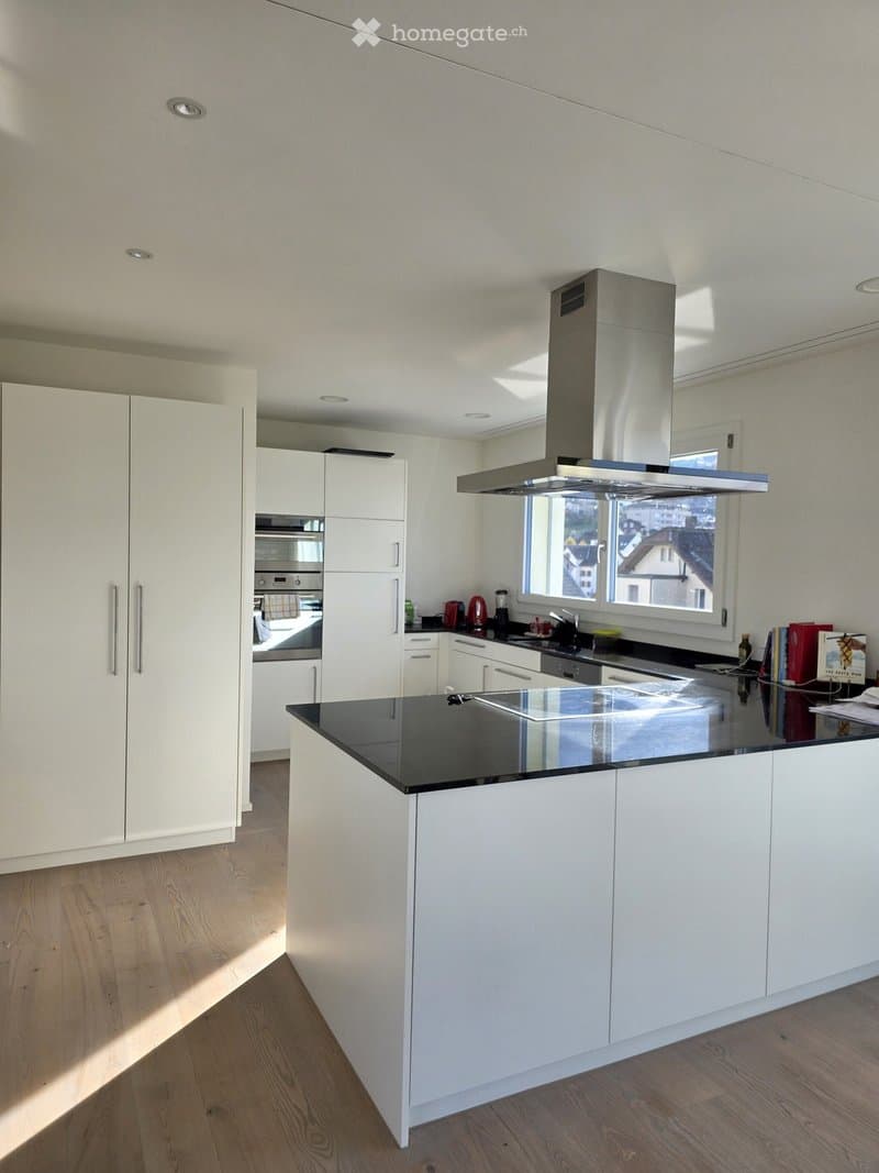 Modern kitchen with white cabinets, black countertop, stainless steel appliances, and a large window offering a view.