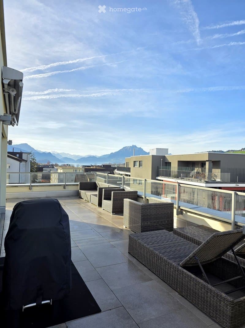 A spacious balcony with wicker seating, a covered grill, and a scenic mountain view.