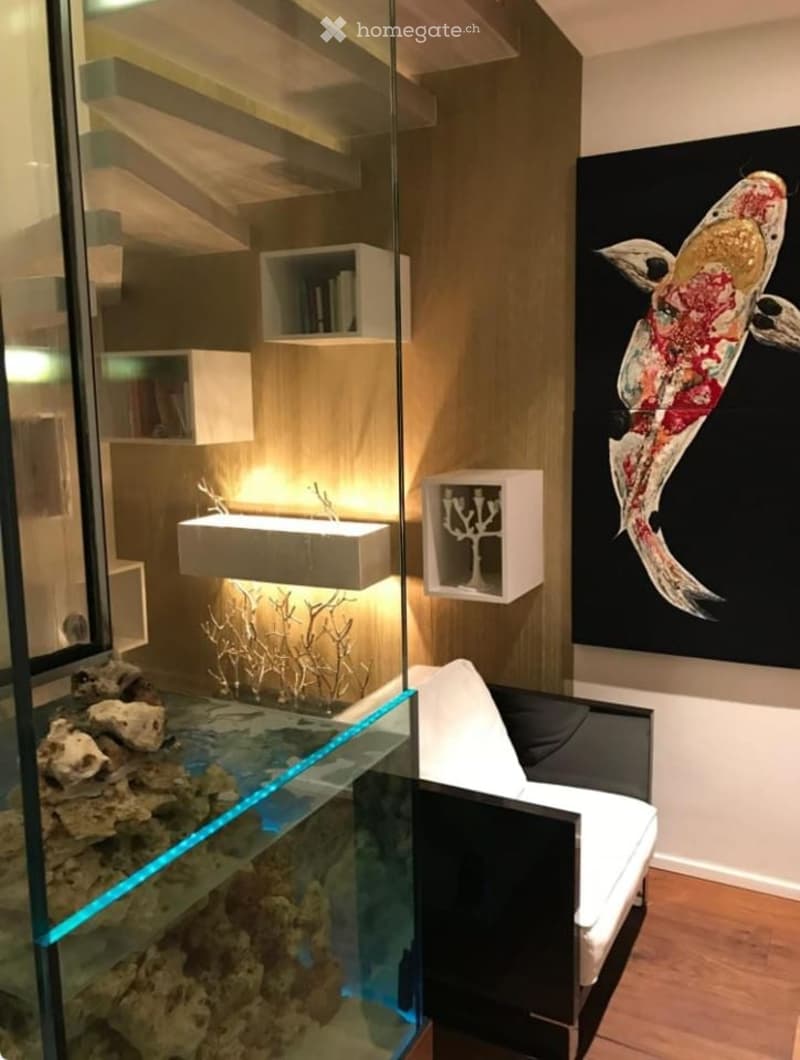 Glass aquarium with fish, white chair, shelves with books and sculptures, wall painting of a koi fish