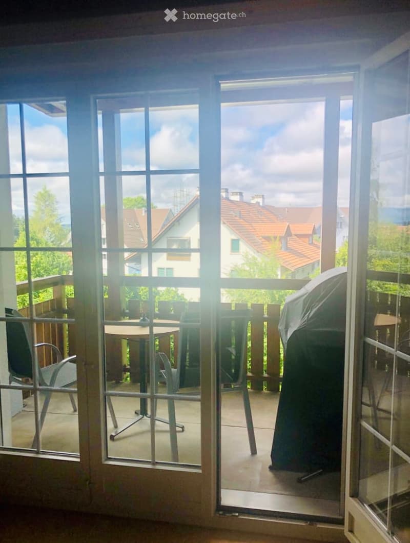 Balcony with a table and chairs, overlooking a residential area with houses and trees.