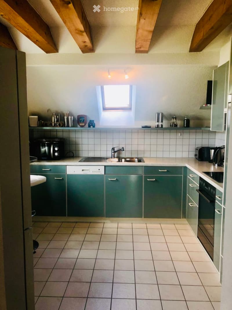 The kitchen features green cabinets, a white tiled floor, and a white countertop. A sink with a faucet is centrally located, and a dishwasher is integrated into the cabinetry. Various appliances, including a toaster and a coffee maker, are placed on the c