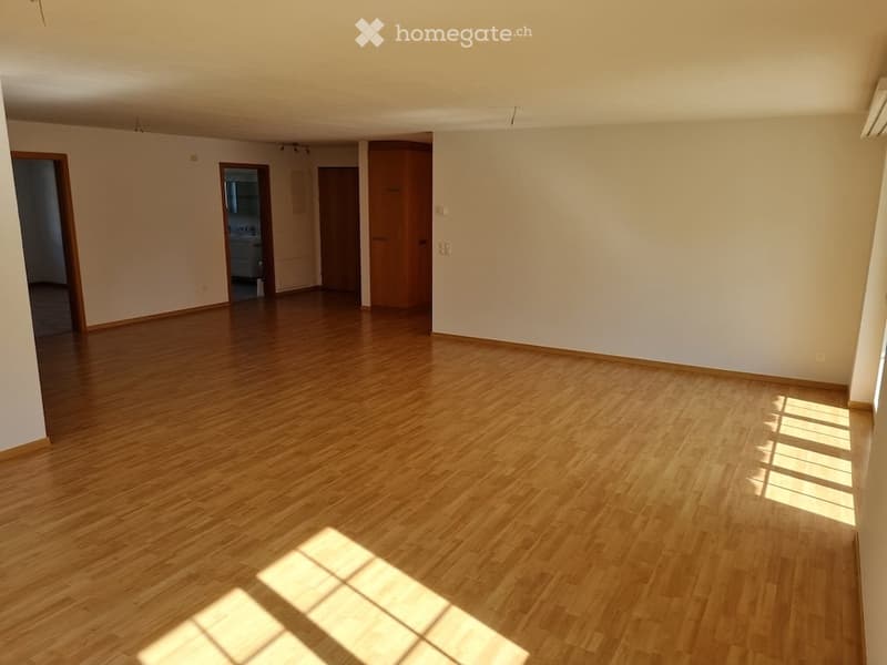 Empty room with wooden flooring and white walls, featuring multiple doors and natural light from a window.