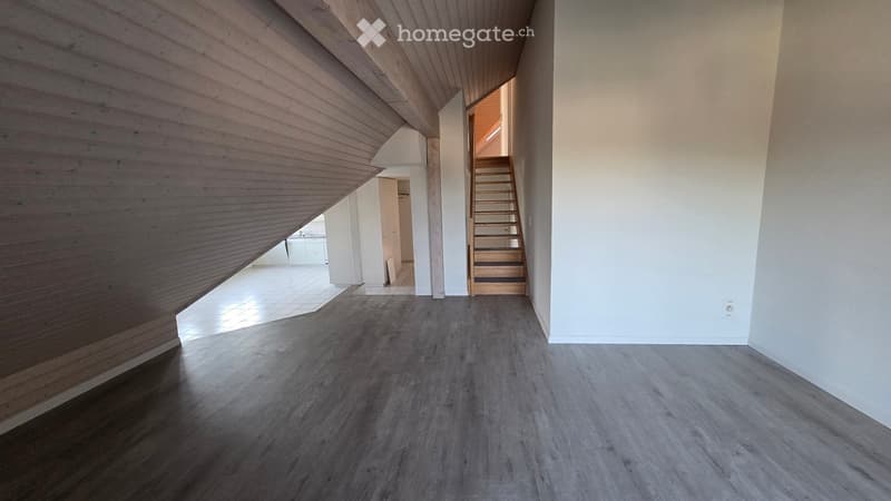 Empty room with wooden flooring and white walls, featuring a staircase leading to another level and an open doorway to another room.