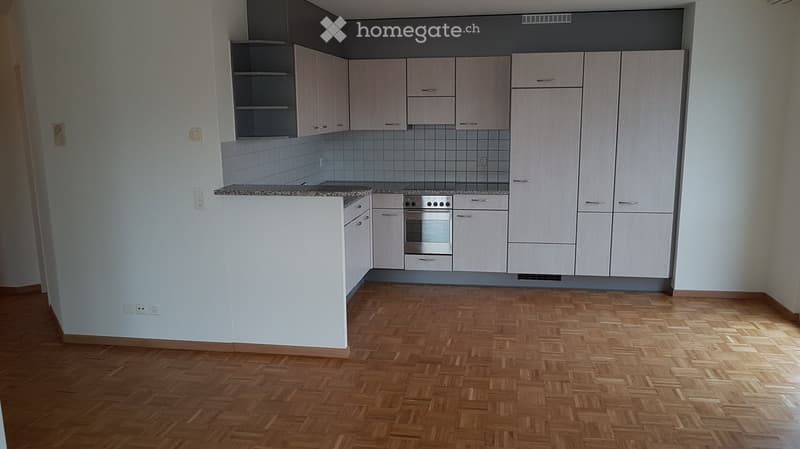 Modern kitchen with light wood cabinets, stainless steel oven, and granite countertop. The floor is made of herringbone-patterned wood.