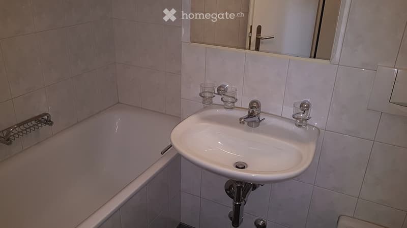 Bathroom with a white sink, faucet, mirror, and bathtub. Several cups are placed on the sink counter.
