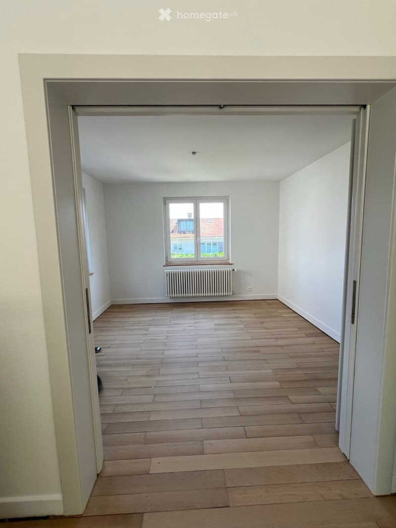 Empty room with wooden flooring, white walls, and a window with a radiator below it.