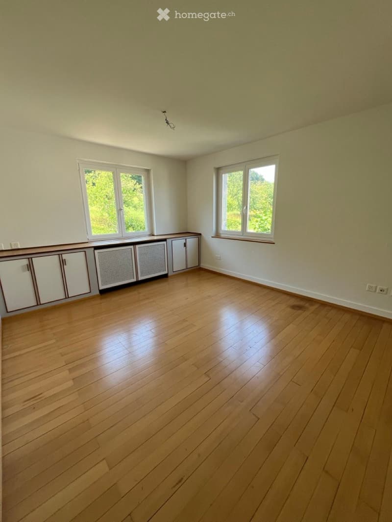 Empty room with wooden flooring, white walls, and built-in cabinets along one wall. Two windows provide natural light.
