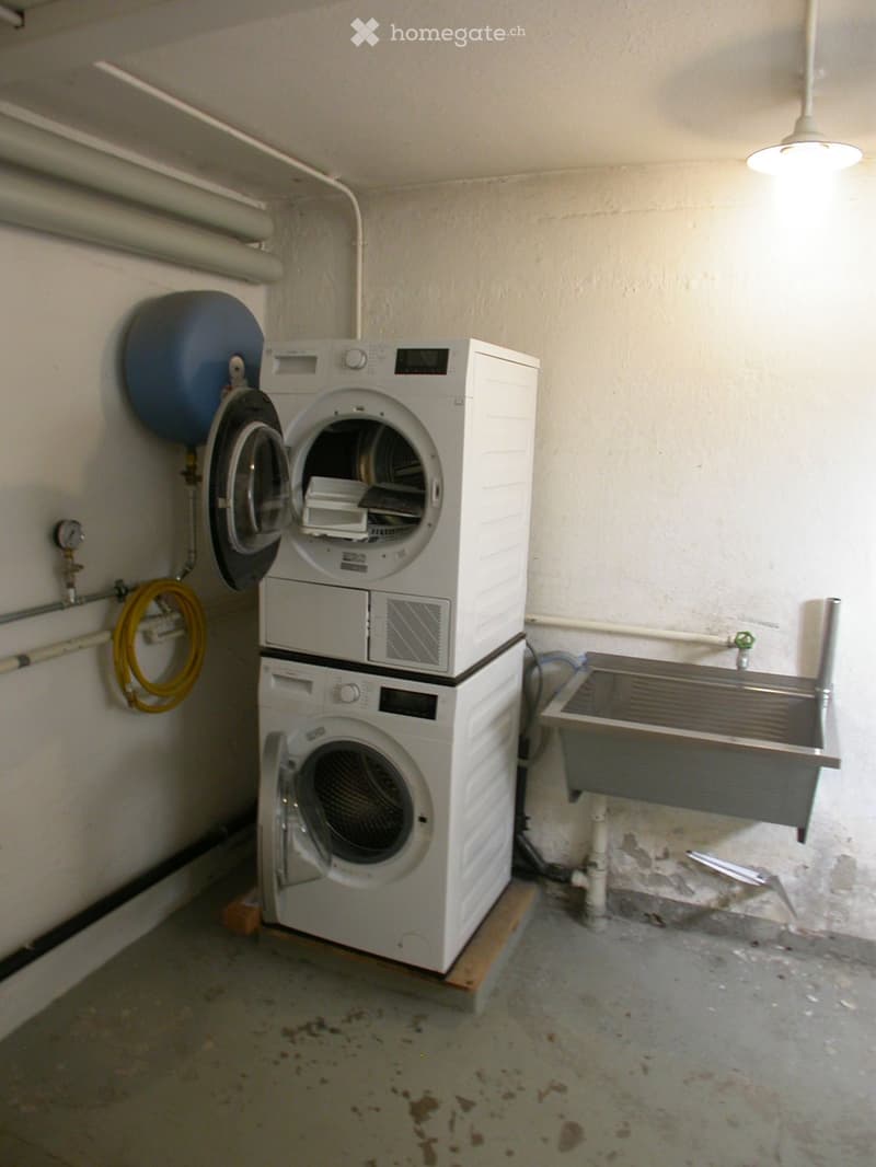 A small utility room with a stacked washing machine and dryer, a sink, and a water heater on the wall.
