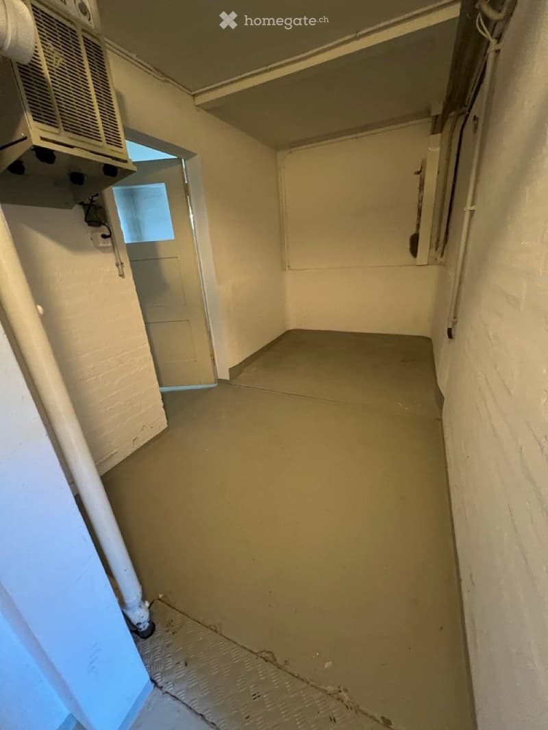 Empty room with bare walls and a concrete floor, featuring a small window and an air conditioning unit on the wall.