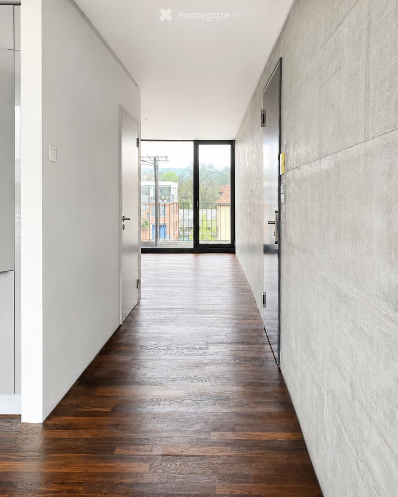 Modern hallway with wooden flooring, white walls, and large glass doors leading to a balcony area.