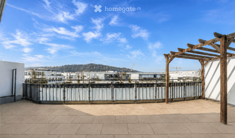 Empty balcony with wooden pergola, metal railing, and tiled floor, overlooking a cityscape with modern buildings and hills.