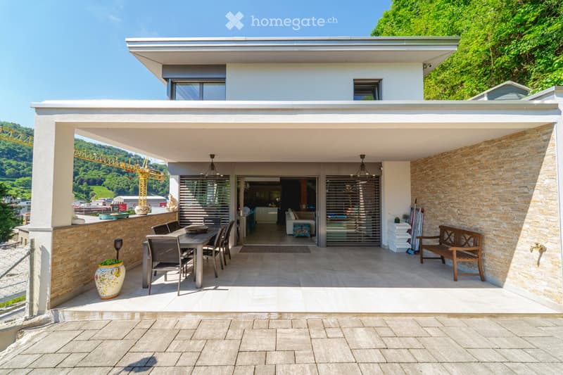 Modern outdoor terrace with a dining set, bench, vase, and view of the city and hills.
