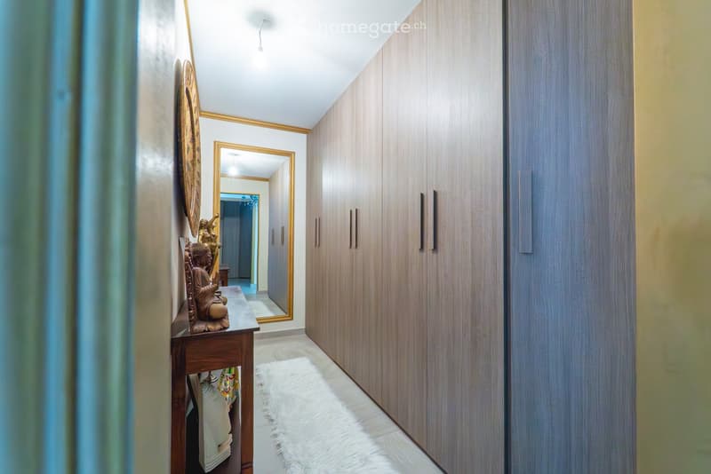A modern hallway with wooden built-in wardrobes, a small wooden table with decorative items, and a large mirror on the wall.