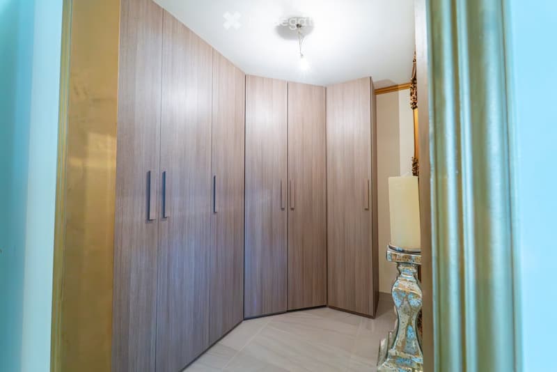 A narrow hallway with modern, light wood paneled walls and matching doors, featuring a decorative table with a candle and a mirror on the right side.
