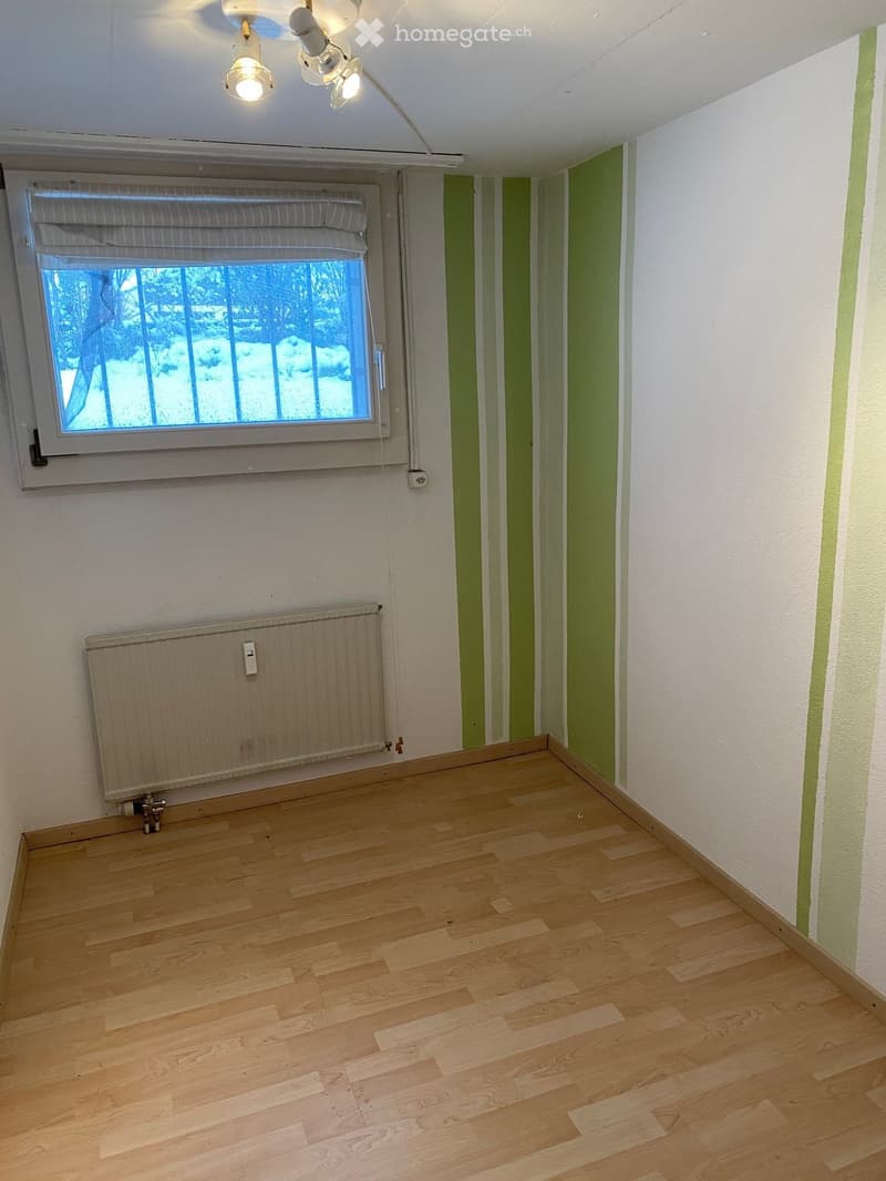 Empty room with wooden flooring, white walls, green accent striping, a window with blinds, and a radiator below the window.