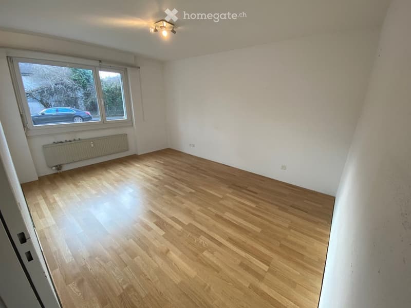 Empty room with wooden flooring, white walls, large window, radiator, and ceiling light fixture.