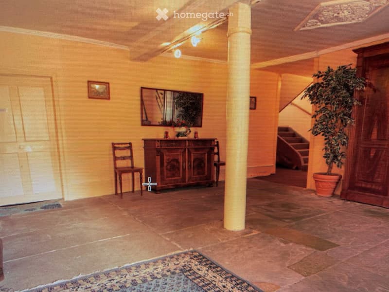 A well-lit hallway with a wooden chair, a cabinet with a mirror, a small table, and a potted plant near the staircase.