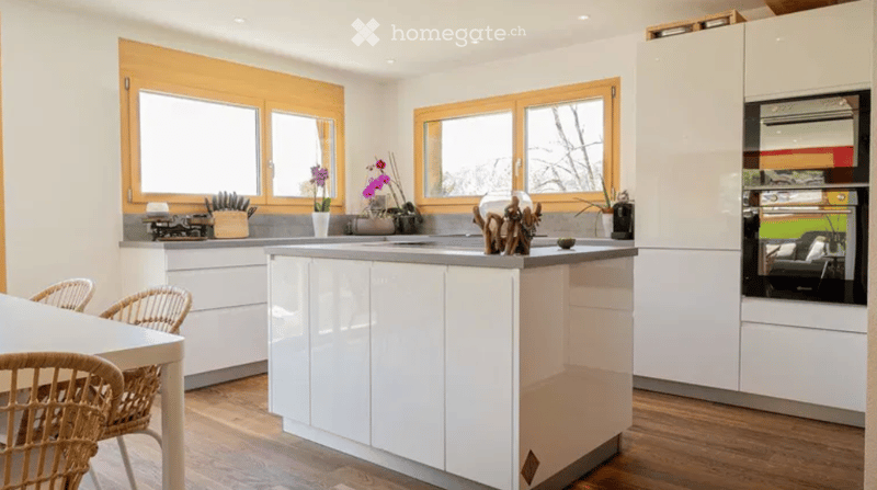 modern kitchen with white cabinets, wooden floor, island with sink, large windows, dining table with chairs