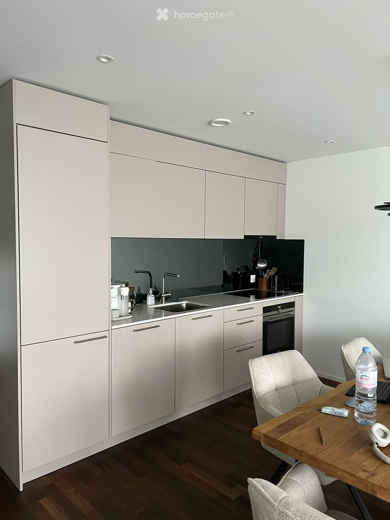 modern kitchen with white cabinets, wooden floor, black countertops, stainless steel sink, faucet, oven, refrigerator, and a dining table with chairs