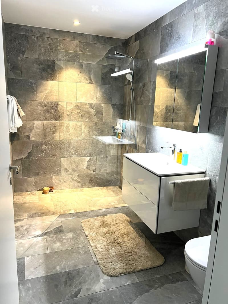 modern bathroom with gray tiles, white vanity, shower with glass door, towel rack, and a toilet