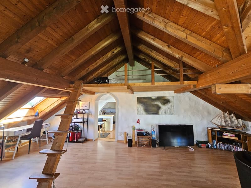 Spacious attic room with wooden beams, hardwood floor, large skylight, TV, model ship, desk, and shelves.