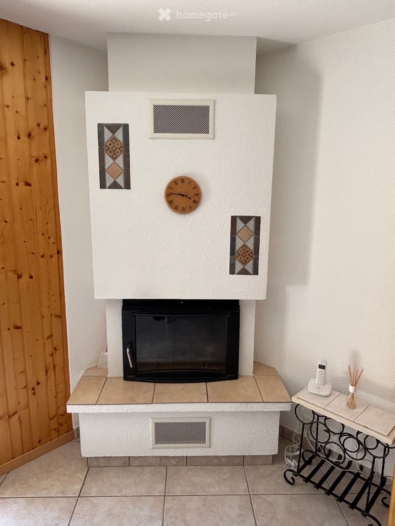 A modern fireplace with a built-in clock, flanked by decorative tiles, and a small table with a telephone and vase nearby.