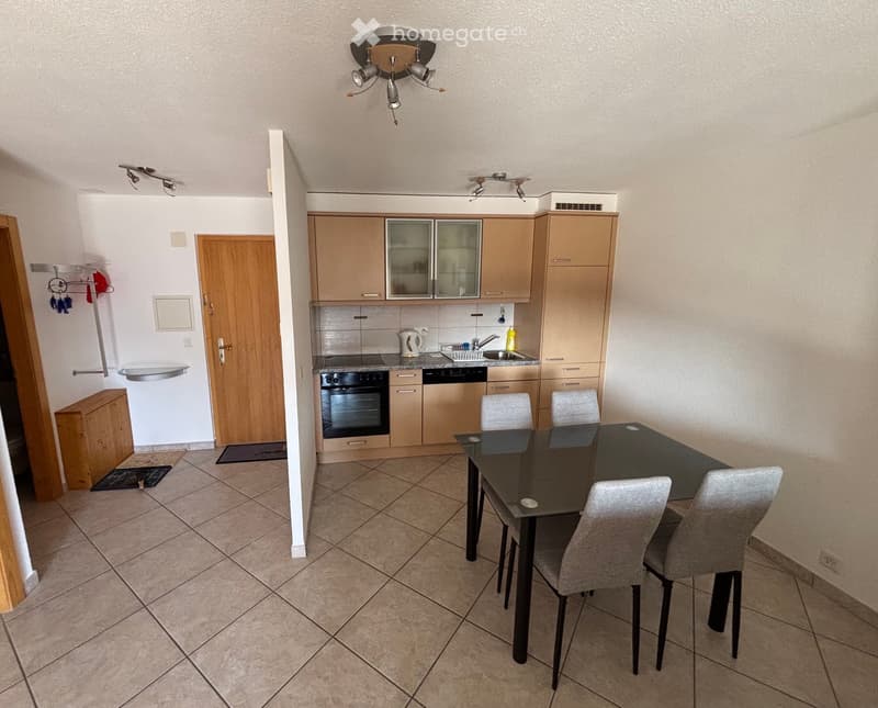 Modern kitchen with light wood cabinets, stainless steel appliances, and a dining area with a black table and four chairs.