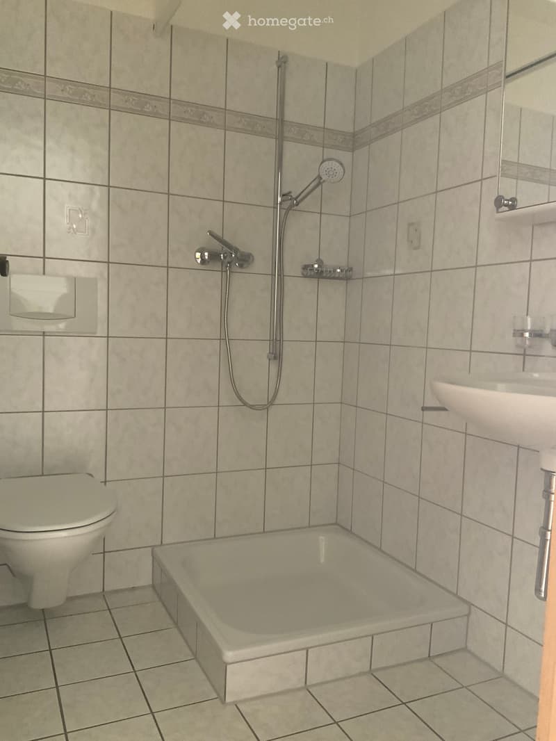 Bathroom with tiled walls and floor, featuring a bathtub, toilet, sink, and showerhead.