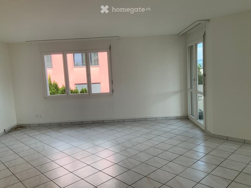 Empty room with tiled floor, white walls, large windows, and a sliding glass door leading outside.