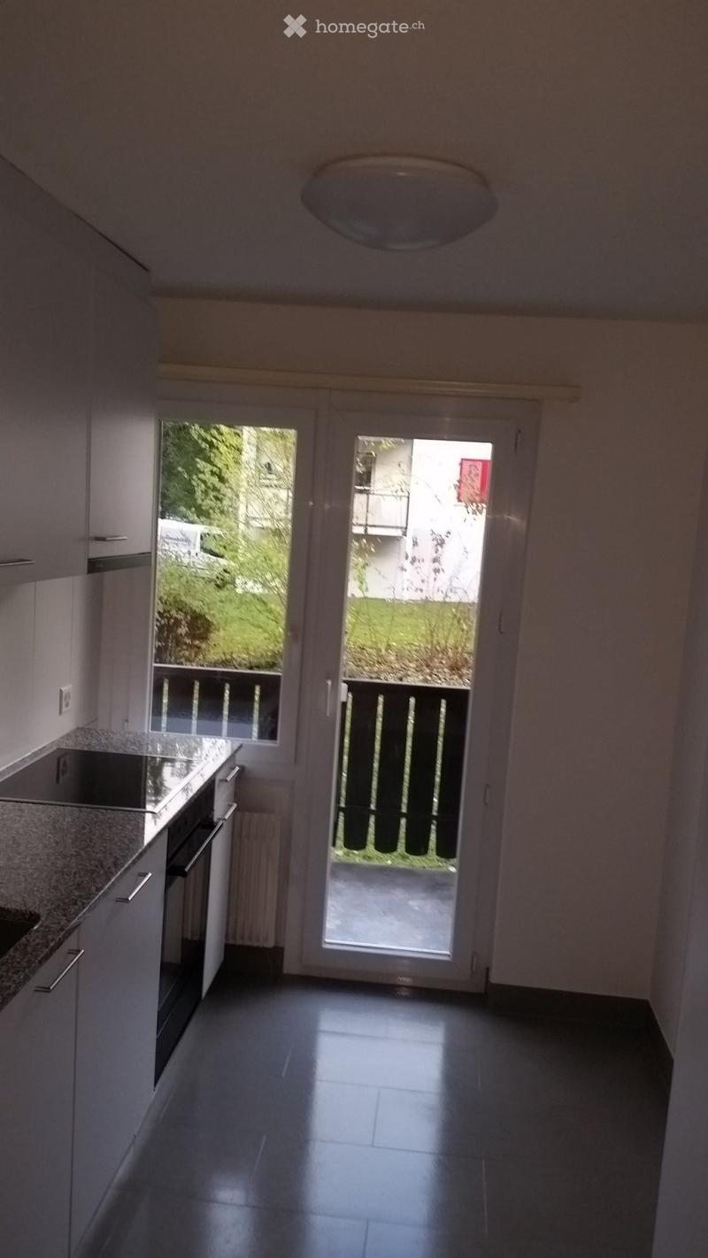 Bright hallway with modern white cabinets, dark tiled floor, and large sliding glass door leading to a balcony with a view of greenery.