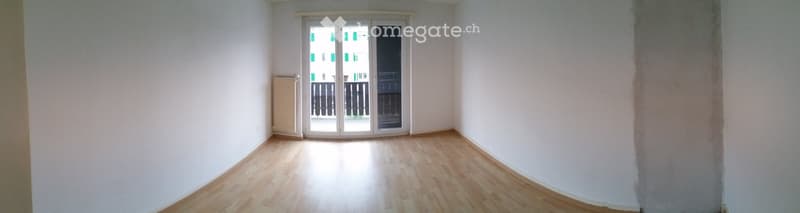 Empty room with wooden flooring, white walls, and a large sliding glass door leading to a balcony.