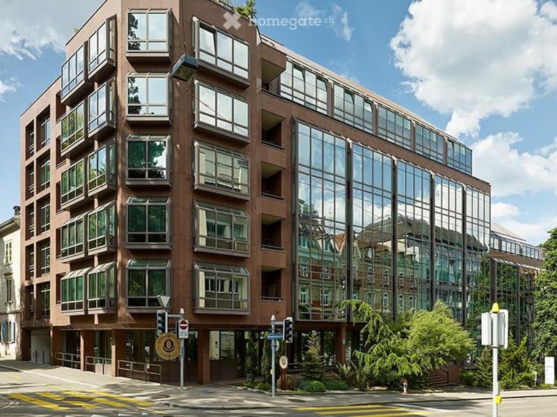 Multi-story building with large windows and balconies, modern design, located on a street with traffic signs and greenery.