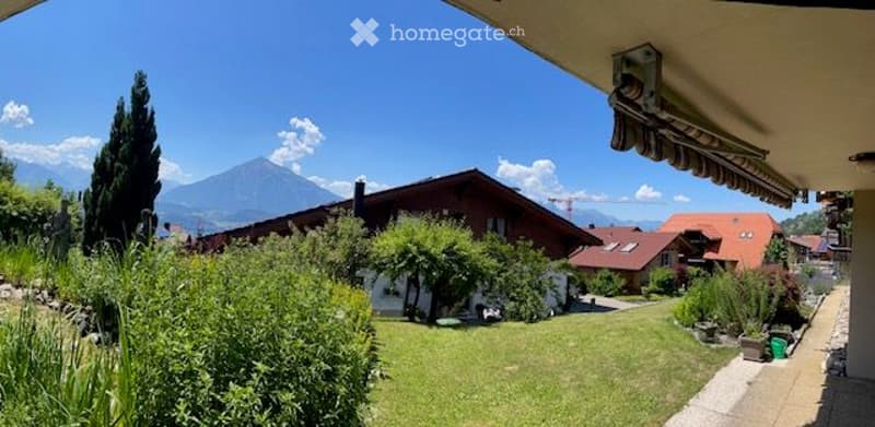 Well-maintained garden with green lawn, trees, and a scenic mountain view in the background.