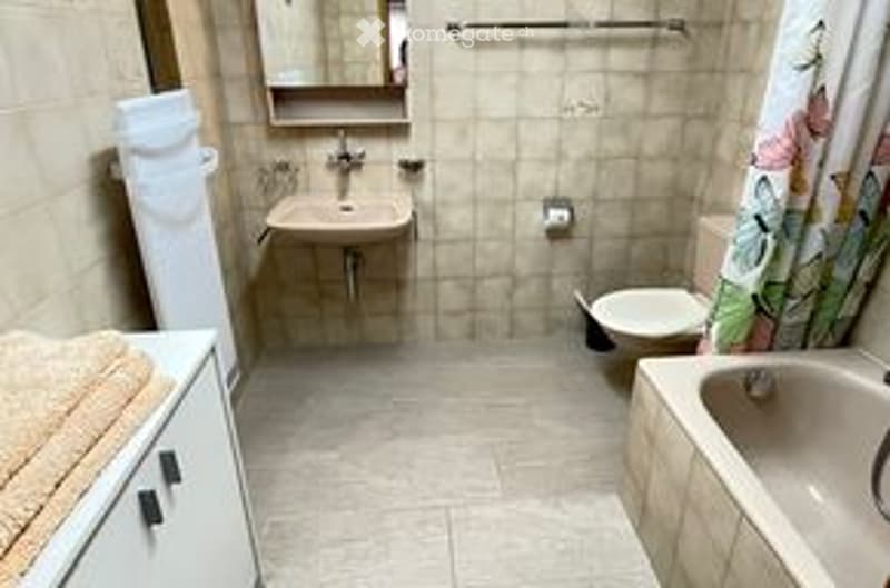 Small bathroom with a sink, toilet, bathtub, and a towel on a cabinet. The walls are tiled, and the floor is also tiled.