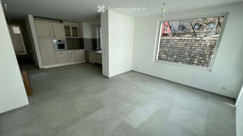 Empty kitchen with white cabinets, stainless steel appliances, and a large window overlooking a tiled roof.