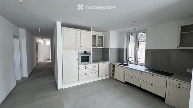Modern kitchen with white cabinets, stainless steel oven, sink, and countertop. Large windows provide natural light.