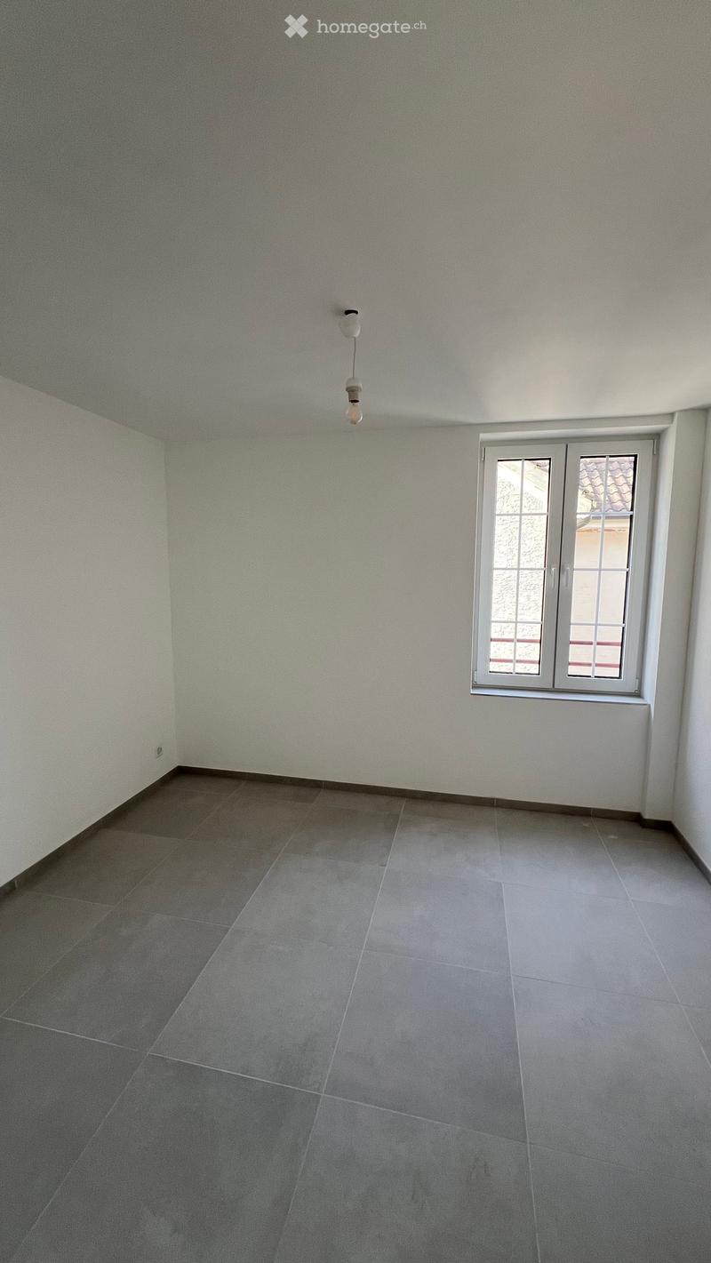 Empty room with grey tiled floor and white walls, featuring a single window with white frame and a hanging light fixture.