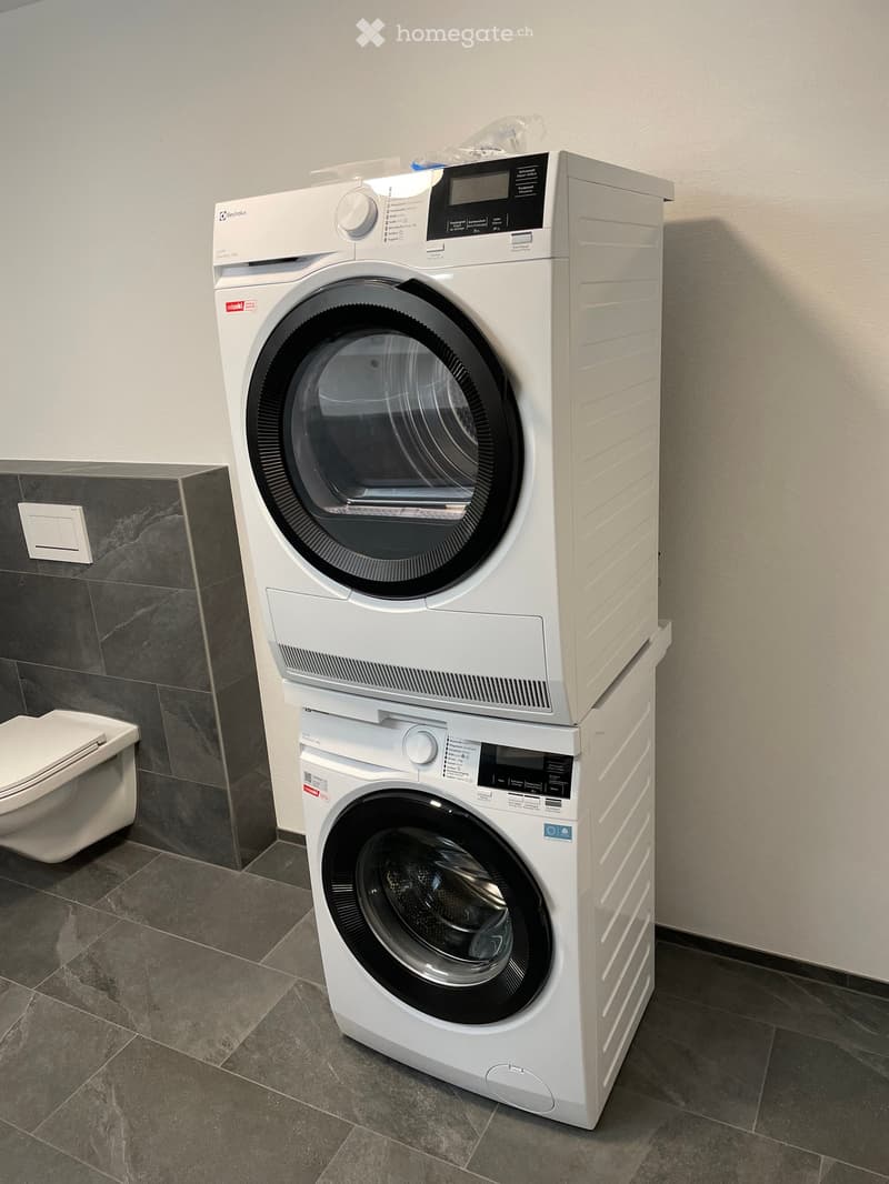Bathroom with a stacked washing machine and dryer unit, a toilet, and tiled walls and floor.