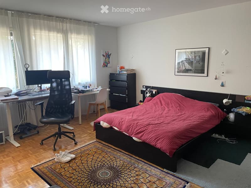 Well-lit bedroom with a double bed, desk, chair, and nightstand. Features a patterned rug, artwork, and a modern aesthetic.