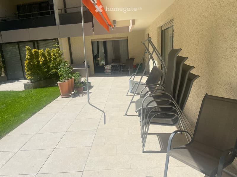 Balcony with tiled floor, several stacked chairs, potted plants, and an orange awning.